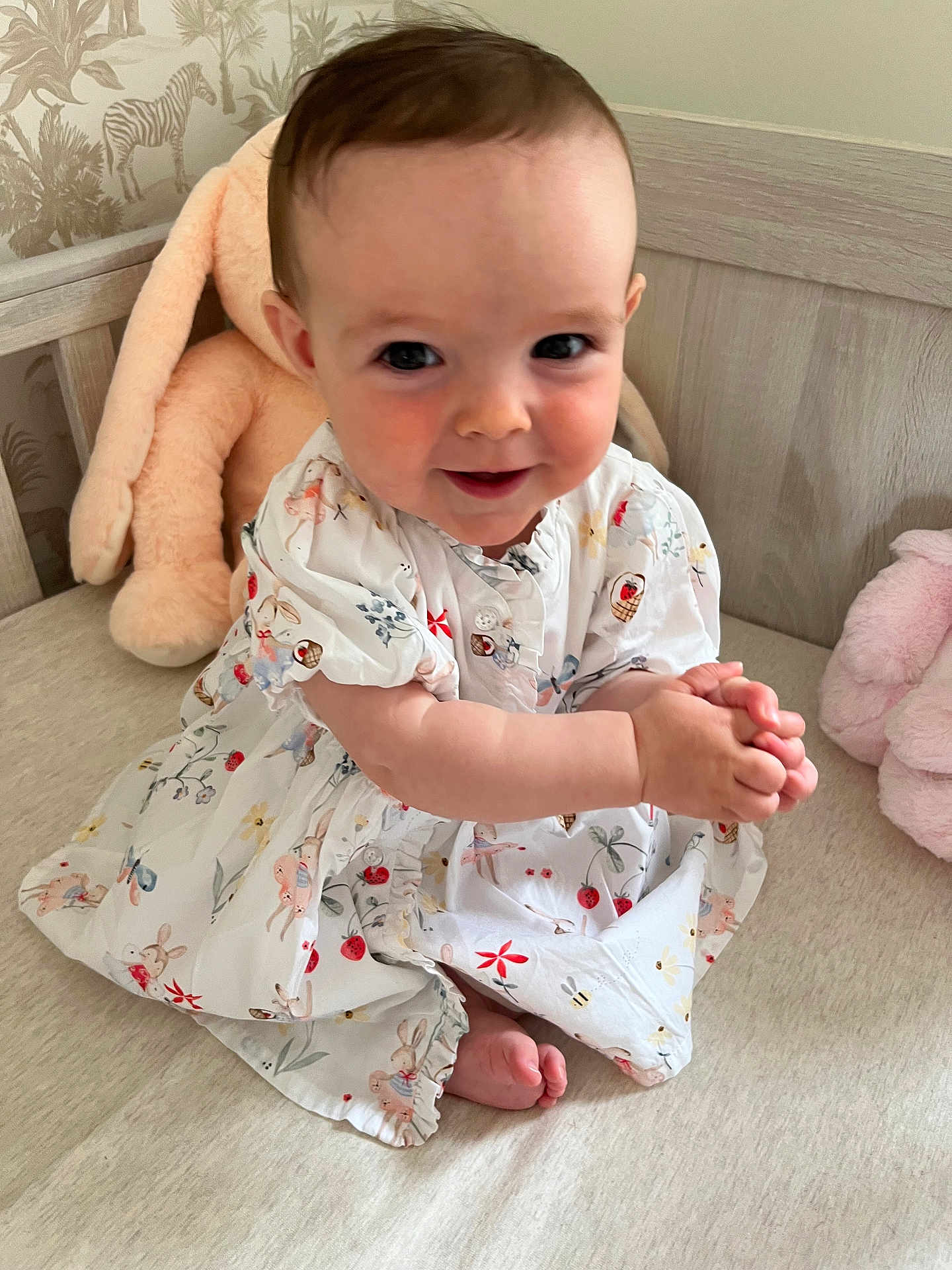Anna is registered to the contest to win money with this photo: baby, child, smiling, dress, clapping, plush_toy, bed, cute, happy, indoor, person, toddler, patterned_clothing, foot, hand, face, head, furniture, soft_toy, infant