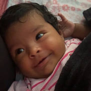 Leslie joined the competition — help win amazing prizes! baby, infant, smile, face, pacifier, blanket, clothing, bed, fabric, curly_hair, cute, lying_down, indoors, person, child, soft, comfort, pink, pattern, young