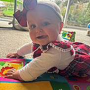 Audrey is registered to the contest to win money with this photo: baby, child, crawling, play_mat, plaid, bow, headband, tongue_out, indoor, carpet, window, garden, cute, smiling, colorful, clothing, person, infant, happy, young_child