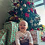Audrey is registered to the contest to win money with this photo: baby, child, christmas_tree, presents, holiday, indoor, carpet, decorations, smile, toy, window, natural_light, festive, red, green, white, brown, portrait, happy, sitting