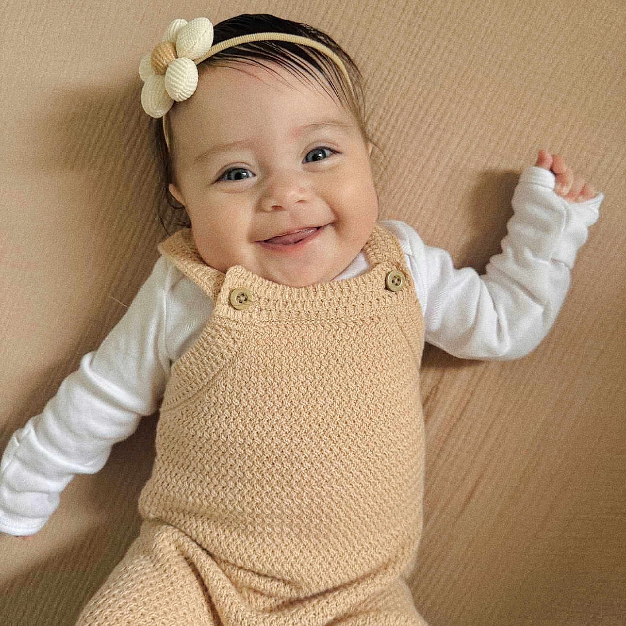 Esther joined the competition — help win amazing prizes! baby, smiling, headband, flower, knitted, overalls, beige, white_shirt, happy, cute, infant, portrait, lying_down, child, face, small_hands, cozy, soft_texture, indoors, person