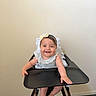 baby, high_chair, smiling, headband, bow, infant, child, furniture, indoor, carpet, wall, clothing, cute, happy, person, portrait, sitting, arm, hand, foot