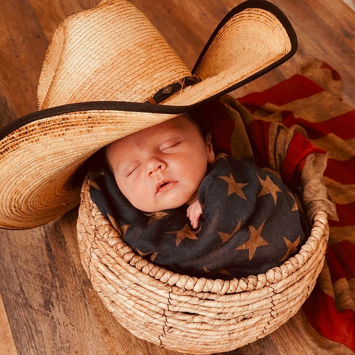 Oliver joined the competition — help win amazing prizes! baby, basket, blanket, child, cowboy_hat, cozy, face, headwear, indoor, infant, newborn, peaceful, plush, portrait, resting, sleeping, star_pattern, wooden_floor, woven, wrapped