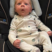 Mav is registered to the contest to win money with this photo: baby, infant, child, car_seat, safety_seat, sitting, wide_eyed, surprised, facial_expression, onesie, clothing, padded_cushion, vehicle_interior, travel, portrait, front_view, indoor, safe, hands, feet
