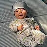 baby, infant, child, portrait, lying_down, onesie, knit_cap, smiling, face, eyes, hands, feet, mattress, bed, textile, indoor, cozy, patterned_clothing, photography, safe