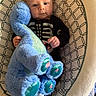 baby, infant, child, plush_toy, blue_dragon, skeleton_shirt, sitting, baby_seat, blanket, patterned_fabric, wide_eyed, portrait, indoors, cozy, toy, blue, black_clothing, hands, face, photography