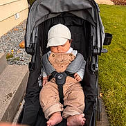 Maverick is registered to the contest to win money with this photo: baby, infant, stroller, sleeping, outdoor, cap, overalls, corduroy, gray_clothing, harness, baby_toys, rattle, grass, walkway, house, garden, portrait, sitting, feet, family_outing