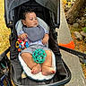 baby, child, stroller, outdoor, park, pathway, tree, leaves, toys, ball, sitting, portrait, face, serious, infant, clothing, bib, striped_shorts, bare_feet, sunlight