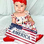 american_flag, baby, celebration, child, cute, dress, expression, footwear, headband, holding, holiday, infant, patriotic, portrait, red_bow, red_shoes, sign, sitting, studio_photo, white_background