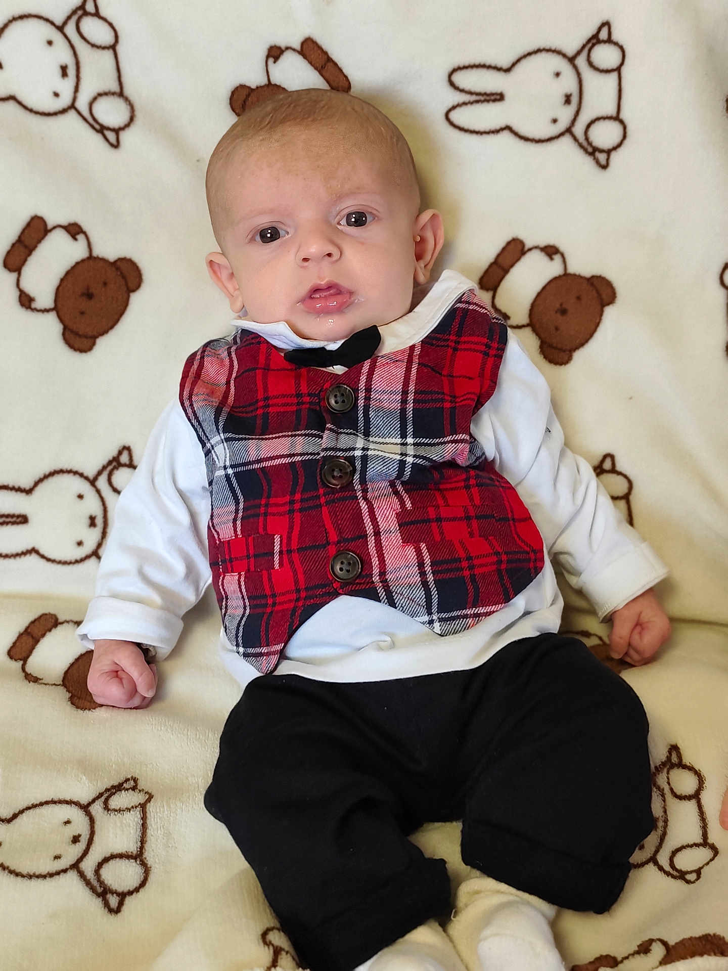 Nolan participe au concours pour gagner de l'argent avec cette photo : baby, infant, plaid_vest, black_pants, white_shirt, blanket, teddy_bear_pattern, bunny_pattern, clothing, cute, portrait, drool, child, indoors, soft_texture, sitting, small_hands, young_child, face, head