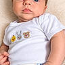 Oliver is registered to the contest to win money with this photo: baby, infant, child, portrait, close_up, lying_down, wide_eyes, blue_eyes, white_clothing, onesie, embroidered_animals, toy_cars, blanket, soft_texture, indoor, adult_hand, newborn, calm, photography, safe