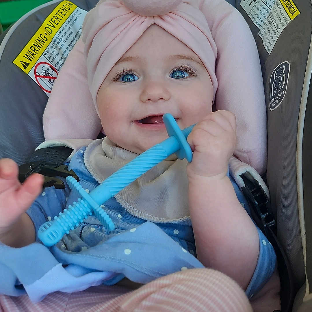 Whitney is registered to the contest to win money with this photo: baby, bib, blue_eyes, car_seat, cheeks, clothing, hand, headwrap, indoor, infant, pink, polka_dot, portrait, safety_label, seatbelt, smile, striped_pants, teether, toy, window