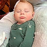 baby, sleeping, onesie, green_clothing, blanket, white_blanket, brown_leather_chair, infant, peaceful, nap, toddler, cute, child, indoor, soft_texture, face, hands_in_pockets, relaxing, portrait, cozy