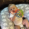 Axl joined the competition — help win amazing prizes! baby, infant, toy, colorful_ball, cushion, elephant_pattern, leather_couch, blanket, smiling, child, indoor, person, playful, cute, white_onesie, relaxed, happy, skin, head, hand