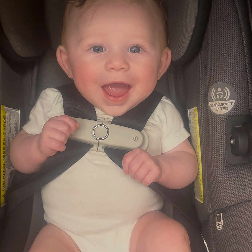 Axl is registered to the contest to win money with this photo: baby, infant, car_seat, smiling, happy, child, safety_harness, cute, blue_eyes, white_onesie, seatbelt, infant_care, child_safety, transportation, car_interior, head_support, young_child, portrait, seated, baby_hands