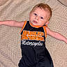 baby, infant, harley_davidson, romper, clothing, couch, furniture, indoor, person, child, cute, arm, face, head, expression, relaxed, comfort, textile, pattern, skin