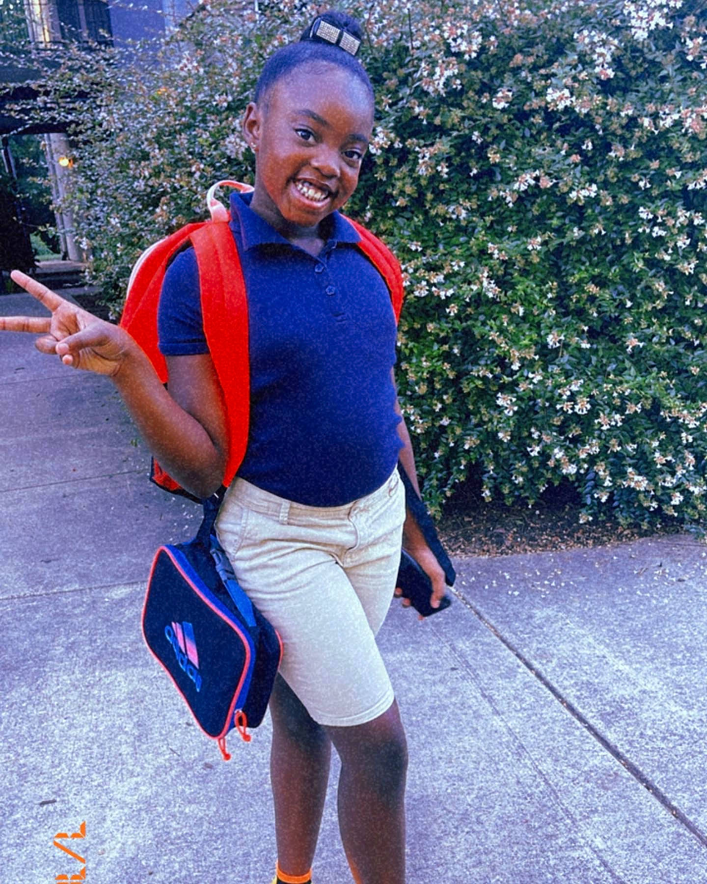 Kennedy is registered to the contest to win money with this photo: bag, chest, cool, electric_blue, eyewear, happy, joy, knee, leisure, luggage_and_bags, person, plant, shorts, shoulder, sleeve, smile, sneakers, sportswear, t_shirt, thigh