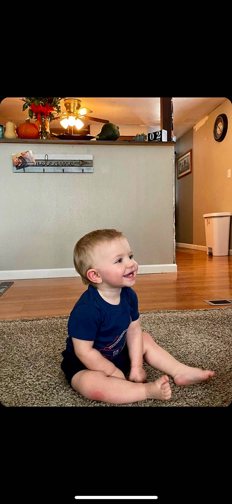 Axell is registered to the contest to win money with this photo: baby, baby_toddler_clothing, child, clock, flash_photography, floor, flooring, fun, hardwood, home_appliance, joy, kitchen_appliance, knee, light, lighting, living_room, person, refrigerator, room, sitting