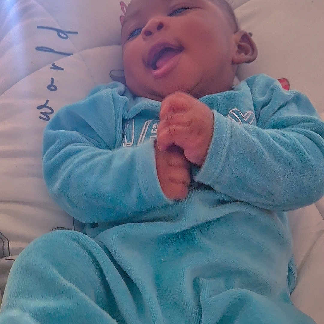 Wiliel participe au concours pour gagner de l'argent avec cette photo : baby, babywear, blue_clothing, child, comfort, cozy, cushion, cute, face, footwear, hand, happy, indoor, infant, person, portrait, relaxing, smiling, soft_light, young