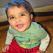Umar joined the competition — help win amazing prizes! toddler, child, smiling, sitting, indoor, floor, wooden_floor, clothing, green_shirt, red_pants, dinosaur_print, cute, happy, face, person, baby, long_sleeves, white_socks, home, bed