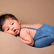 Jaycob is registered to the contest to win money with this photo: baby, infant, newborn, blue_outfit, knitted_clothing, soft_texture, curly_hair, lying_down, beige_background, cute, chubby_cheeks, portrait, child, skin, face, expression, resting, small_feet, indoors, cozy