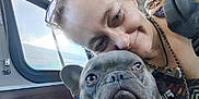 Smokey is registered to the contest to win money with this photo: woman, dog, french_bulldog, face, pet, smile, bus, window, glasses, chain_necklace, public_transport, seated, daylight, portrait, closeup, indoor, person, canine, animal, transportation