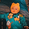 baby, child, bed, blue_bedspread, yellow_hat, disney_characters, mickey_mouse, donald_duck, pluto, clothing, sweater, pants, indoor, portrait, infant, cute, lying_down, person, face, headwear