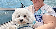 Tina a rejoint le concours — aidez-le/la à gagner de superbes lots ! dog, person, boat, ocean, water, fishing, fishing_rod, pet, white_dog, curly_fur, fluffy, life_jacket, bucket_hat, floral_hat, outdoor, sunny, portrait, smiling, sea, companion