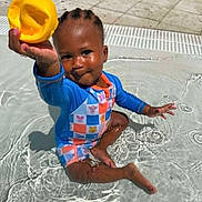 Malakai joined the competition — help win amazing prizes! toddler, child, pool, water, swimming, outdoor, sunlight, yellow_scoop, toy, smiling, sitting, wet, playful, blue_clothing, striped_outfit, braids, pavement, tiles, summer, portrait