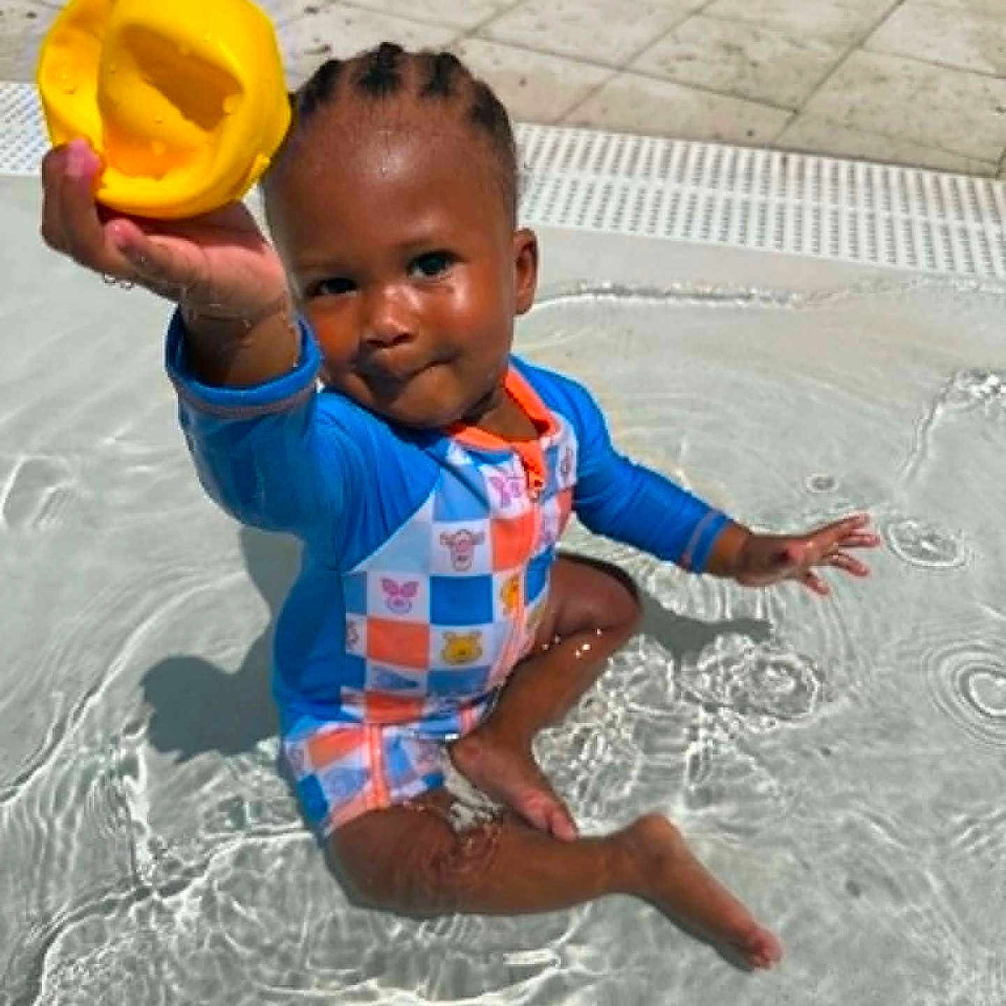 Malakai joined the competition — help win amazing prizes! toddler, child, pool, water, swimming, outdoor, sunlight, yellow_scoop, toy, smiling, sitting, wet, playful, blue_clothing, striped_outfit, braids, pavement, tiles, summer, portrait