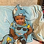 baby, child, smiling, sitting, blue_outfit, hat, blanket, indoor, cute, happy, person, clothing, cartoon_characters, infant, toddler, face, headwear, cozy, comfort, portrait