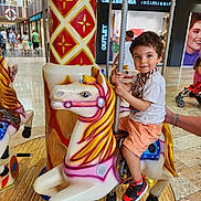 Leo participe au concours pour gagner de l'argent avec cette photo : adult_hand, background, boy, carousel, child, clothing, colorful, floor, fun, horse, indoor, people, play, pole, ride, shoes, shopping_mall, smile, store, toy