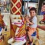 adult_hand, background, boy, carousel, child, clothing, colorful, floor, fun, horse, indoor, people, play, pole, ride, shoes, shopping_mall, smile, store, toy