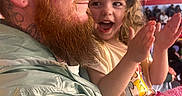 Aylani joined the competition — help win amazing prizes! child, man, beard, glasses, cap, clapping, happy, smile, curly_hair, indoor, crowd, jacket, pink_blanket, person, family, portrait, closeup, excitement, seated, casual_clothing