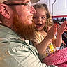 child, man, beard, glasses, cap, clapping, happy, smile, curly_hair, indoor, crowd, jacket, pink_blanket, person, family, portrait, closeup, excitement, seated, casual_clothing