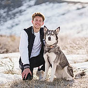 Legacy is registered to the contest to win money with this photo: man, dog, husky, snow, outdoor, smiling, winter, nature, grass, portrait, kneeling, animal, pet, young_adult, casual_clothing, collar, field, daylight, fur, happy