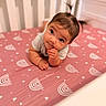 baby, bedroom, child, crib, curious, eyes, face, fingers, hair, hand, indoors, infant, lying_down, mattress, nursery, pigtails, pink, portrait, rainbow_pattern, sitting