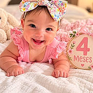 Angelica joined the competition — help win amazing prizes! baby, infant, child, smiling, portrait, floral_bow, pink_outfit, blanket, bed, cozy, indoor, bedroom, milestone, four_months, birthday_sign, floral_decoration, happy, sitting, close_up, soft_lighting