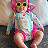 baby, infant, child, sunglasses, hat, colorful_clothing, seashell_pattern, floral_pattern, sitting, couch, pillow, indoor, portrait, smiling, fashion, costume, bright_colors, baby_photography, legs, playful