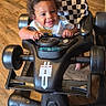 baby, child, indoor, floor, walker, toy, smile, happy, person, curly_hair, black, checkered, seat, wooden_floor, furniture, living_room, play, cute, toddler, baby_walker