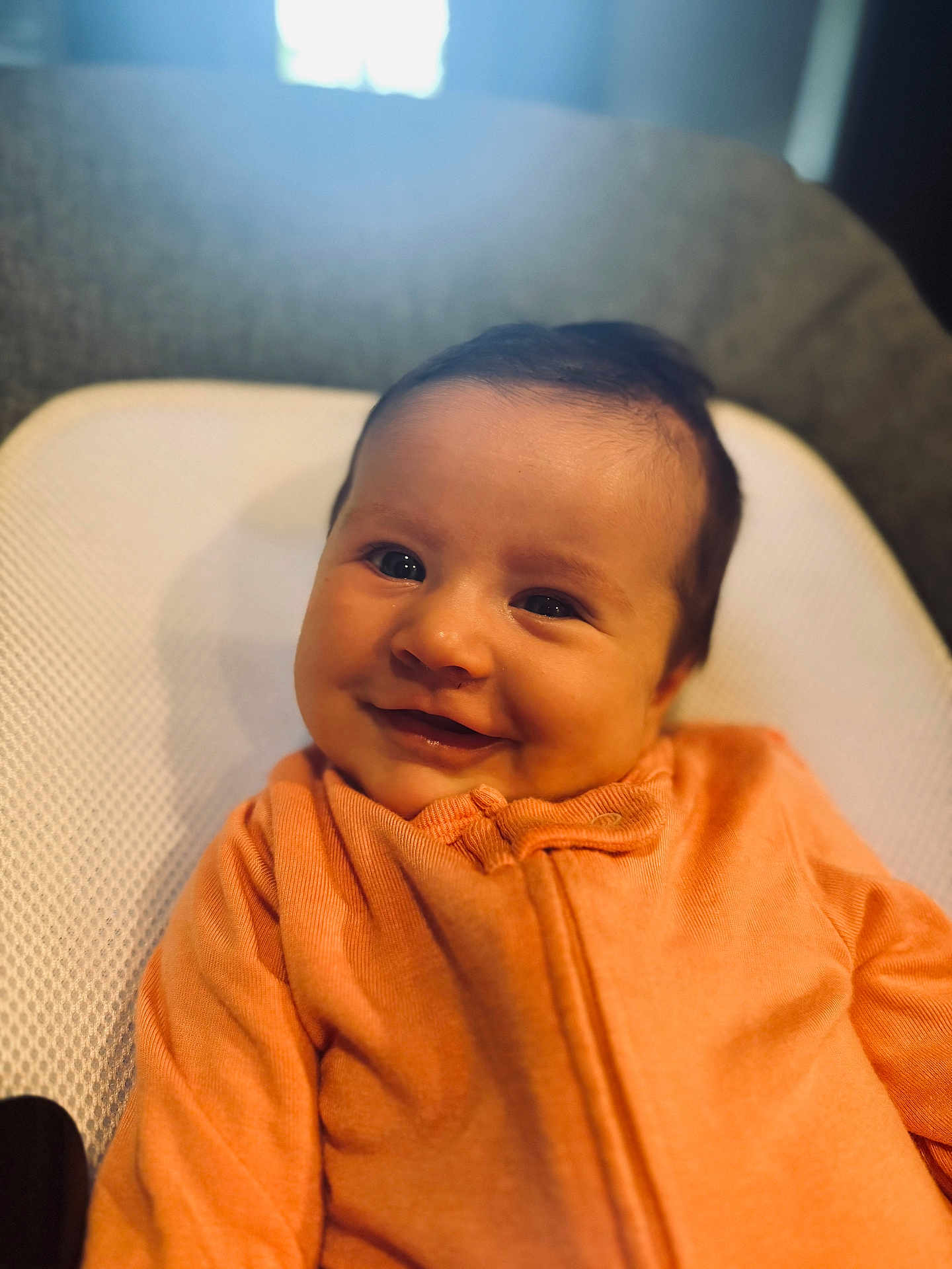 Ella is registered to the contest to win money with this photo: baby, smiling, infant, orange_clothing, cushion, white_background, portrait, happy, child, face, head, closeup, indoors, soft_light, cute, young_child, seated, textile, warm_colors, baby_garment