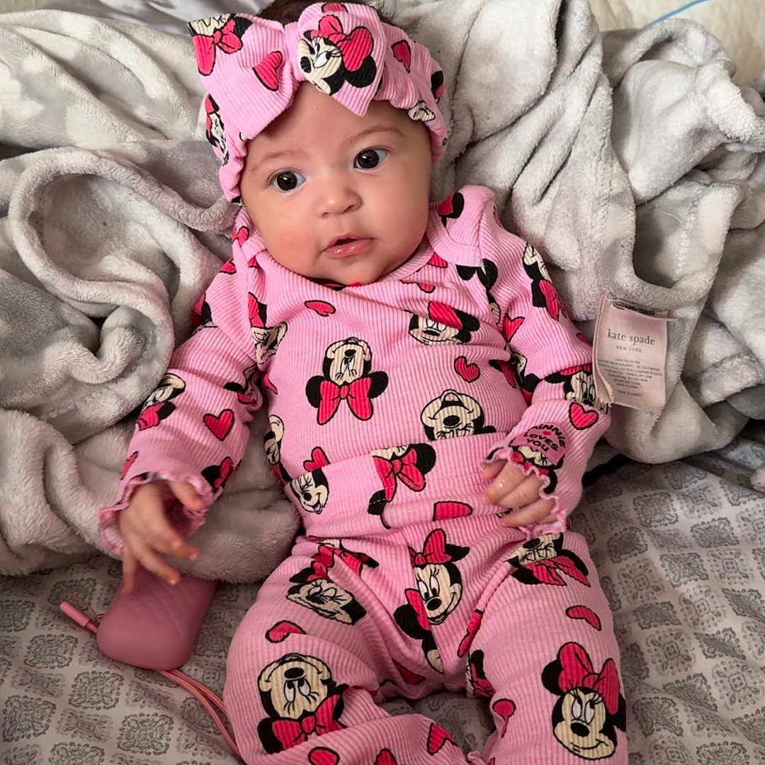 Aurora joined the competition — help win amazing prizes! baby, bed, blanket, child, comfort, cozy, cute, headband, indoors, infant, minnie_mouse, patterned_sheet, person, pink_clothing, portrait, resting, sleepwear, socks, soft_texture, young_child