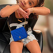 Cataleya Falcon joined the competition — help win amazing prizes! child, girl, curly_hair, black_top, denim_shorts, blue_purse, gold_bracelet, black_sandals, chair, posing, smiling, indoor, cute, fashion, accessories, portrait, young_child, sitting, casual, happy