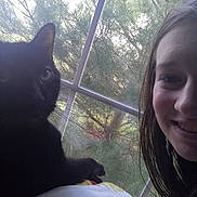 Cooper is registered to the contest to win money with this photo: animal, black_cat, blanket, cat, cozy, curious, face, feline, greenery, home, indoor, natural_light, person, pet, portrait, relaxed, resting, screen, smiling, window