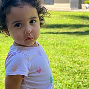 Alessia joined the competition — help win amazing prizes! background_blur, casual_clothing, child, curly_hair, cute, daylight, expression, face, grass, heart_pattern, looking, nature, outdoor, person, portrait, shirt, standing, sunlight, toddler, young_child
