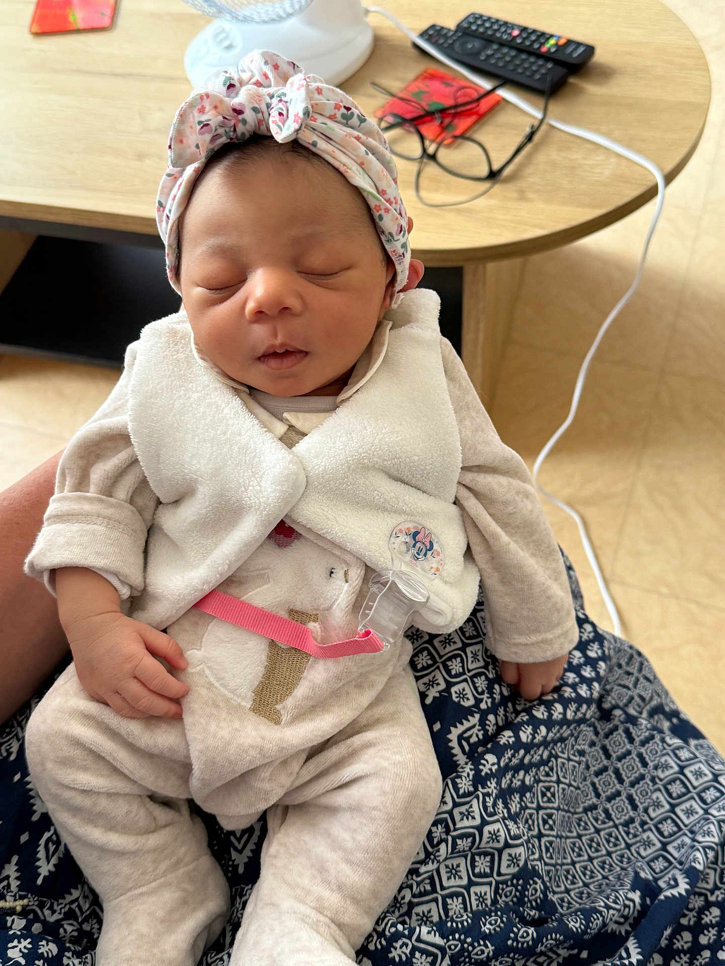 Inaya a rejoint le concours — aidez-le/la à gagner de superbes lots ! baby, infant, sleeping, headband, vest, onesie, hand, patterned_cloth, table, remote_control, glasses, pacifier_clip, floor, indoors, person, cute, peaceful, closeup, soft_fabric, resting