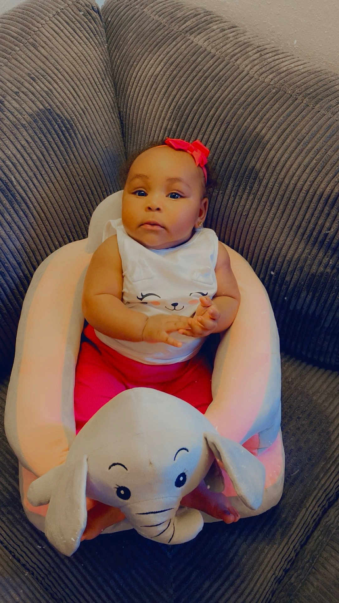 Michelle joined the competition — help win amazing prizes! baby, child, pink_bow, elephant_plush, plush_seat, couch, indoor, cute, infant, clothing, white_shirt, red_pants, smiling_face, portrait, sitting, soft_furniture, home, cozy, adorable, young_child