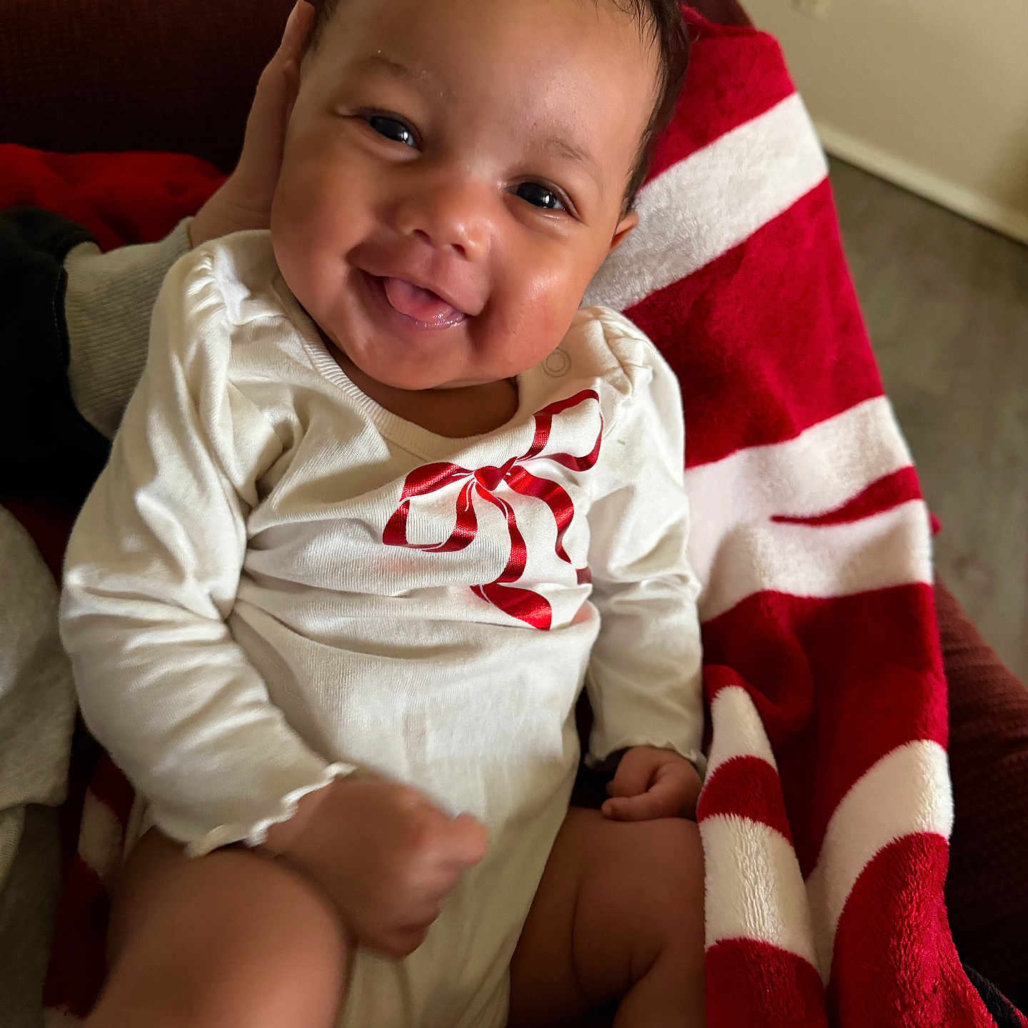 Alani is registered to the contest to win money with this photo: baby, blanket, child, cozy, cute, face, hand, happy, indoors, infant, leg, person, portrait, red_and_white, red_bow, sitting, skin, smiling, toddler, white_clothing