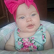 Eliana is registered to the contest to win money with this photo: baby, child, headband, bow, pink, floral_dress, cushion, seat, indoor, face, chubby_cheeks, curious, person, portrait, infant, cute, skin, young_child, happy, clothing