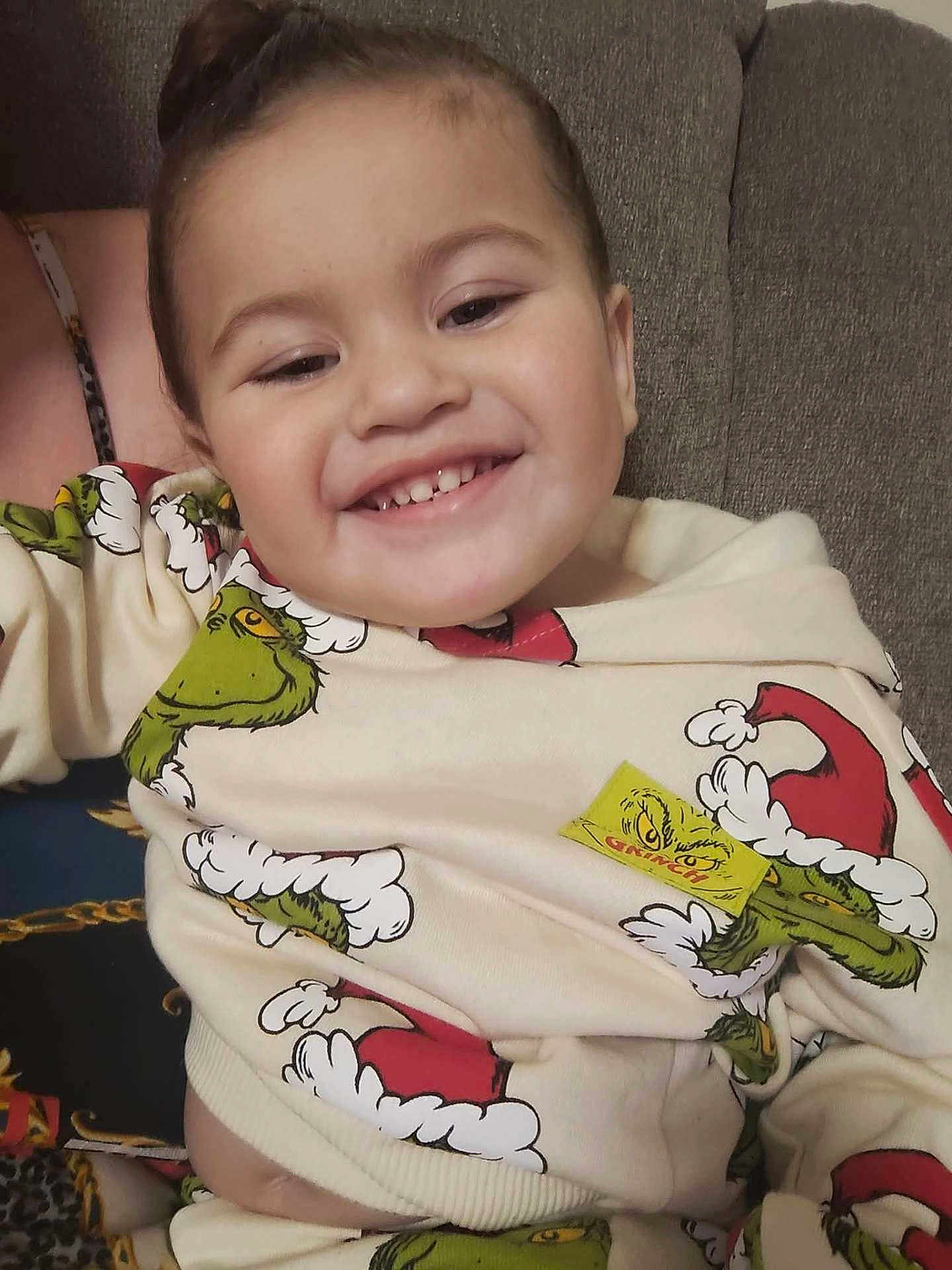 Junior is registered to the contest to win money with this photo: toddler, child, smile, grinch, sweater, clothing, happy, face, couch, indoor, person, portrait, cozy, seated, apparel, cute, young_child, sitting, warm, relaxed